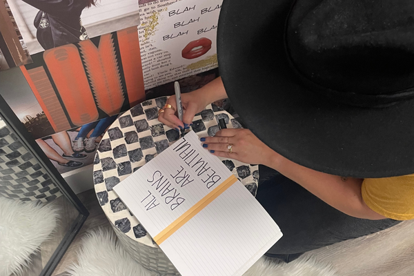 A woman writing in a journal that reads, "All brains are beautiful," a statement of support for neurodiversity