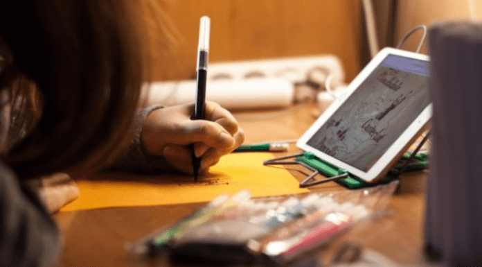 Communication: 7 Conversation Starters For Kids A child sitting in front of a tablet at a table, writing with a marker