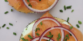 A sliced bagel topped with cream cheese, nova, and sliced red onions