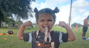 Little girl biting a soccer medal and showing her muscles