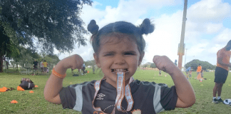 Little girl biting a soccer medal and showing her muscles