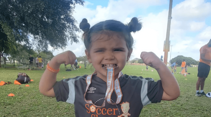 Little girl biting a soccer medal and showing her muscles