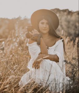 Coco sitting in a field, holding a camera