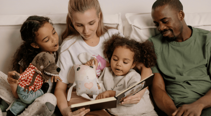 Children’s Books For Black History Month Image: A multi-racial family sitting a reading a book together