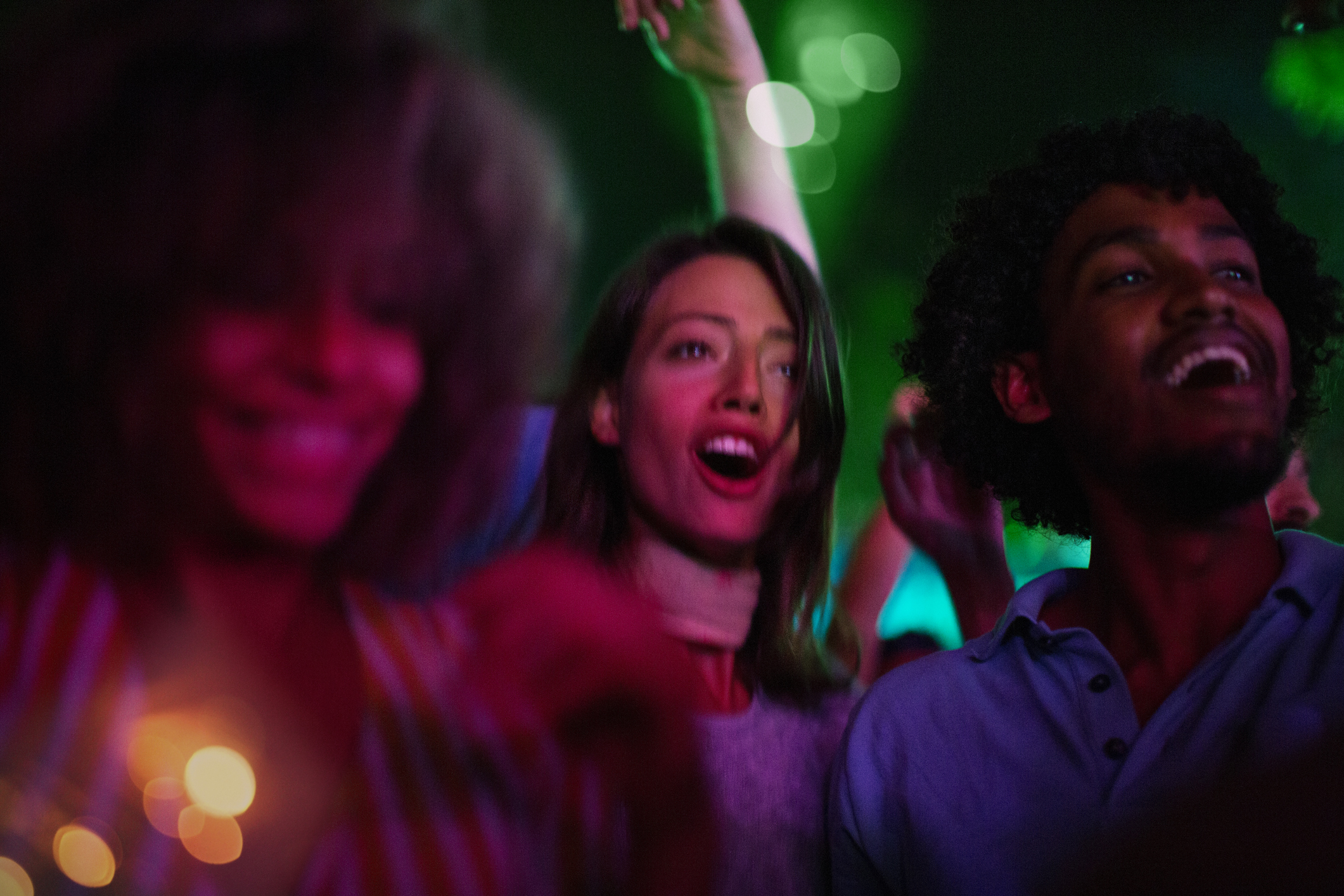 Four Weekends for Your Five Senses: Miami Beach Live Miami Mom Collective Friends with arms raised dancing and singing at music festival. They are illuminated with red and green stage light.