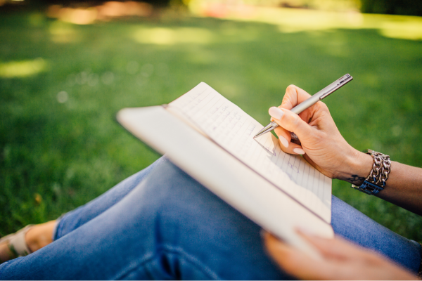 Image: A woman sitting in the grass, writing in her journal