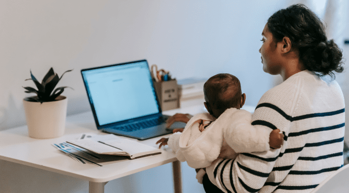 Image: A mom holding her baby while she works at her computer (5 Tips for the Momtrepreneur Minnie Roca Contributor Miami Mom Collective)