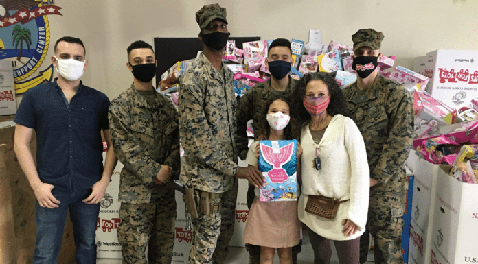 Image: Adita and her daughter with several US Marines standing in front of Toys for Tots collection boxes (Toys for Tots: Making a Difference for America's Children Adita Lang Contributor Miami Mom Collective)