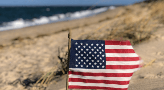Image: An American flag in the sand with the ocean behind it