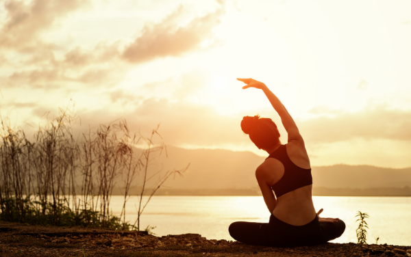 Image: A woman stretches by a lake (Minimize Stress: 18 Helpful Tips Lorena Lougedo Contributor Miami Mom Collective)