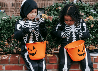 Allergy-Friendly Halloween: Tricks and Treats Image: Two girls in skeleton costumes sitting with their Halloween buckets