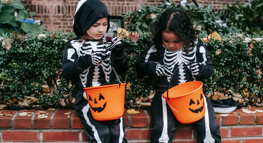 Image: Two girls in skeleton costumes sitting with their Halloween buckets