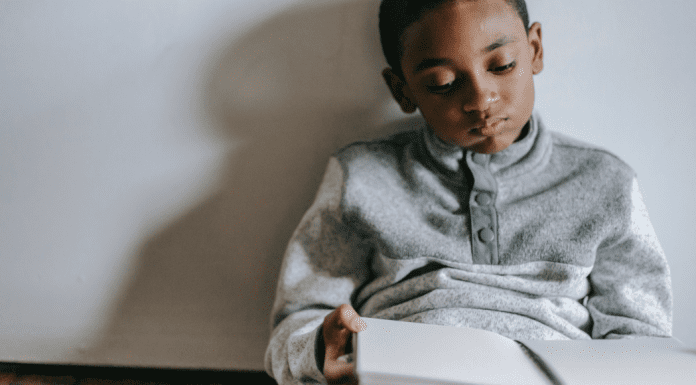 Stuck Inside? Try These Gross Motor Games! Image: A boy sitting with a book in his lap (Stuck Inside? Try These Gross Motor Games! Brittany Aquart Contributor Miami Mom Collective)