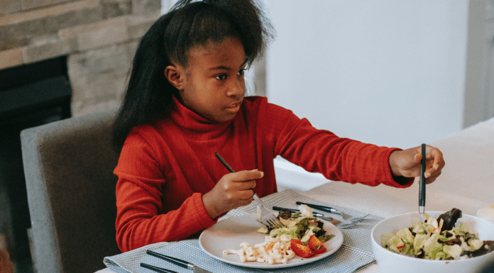 Raising a Diverse Eater: 3 Keys to Success Image: A school-aged girl sitting at a table eating (Raising a Diverse Eater: 3 Keys to Success Dina Garcia Contributor Miami Mom Collective)