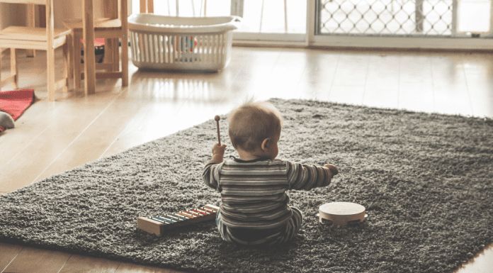 Baby Equipment: What to Avoid and Better Alternatives A baby playing on a grey rug in a minimalist room. The baby is playing with musical toys.