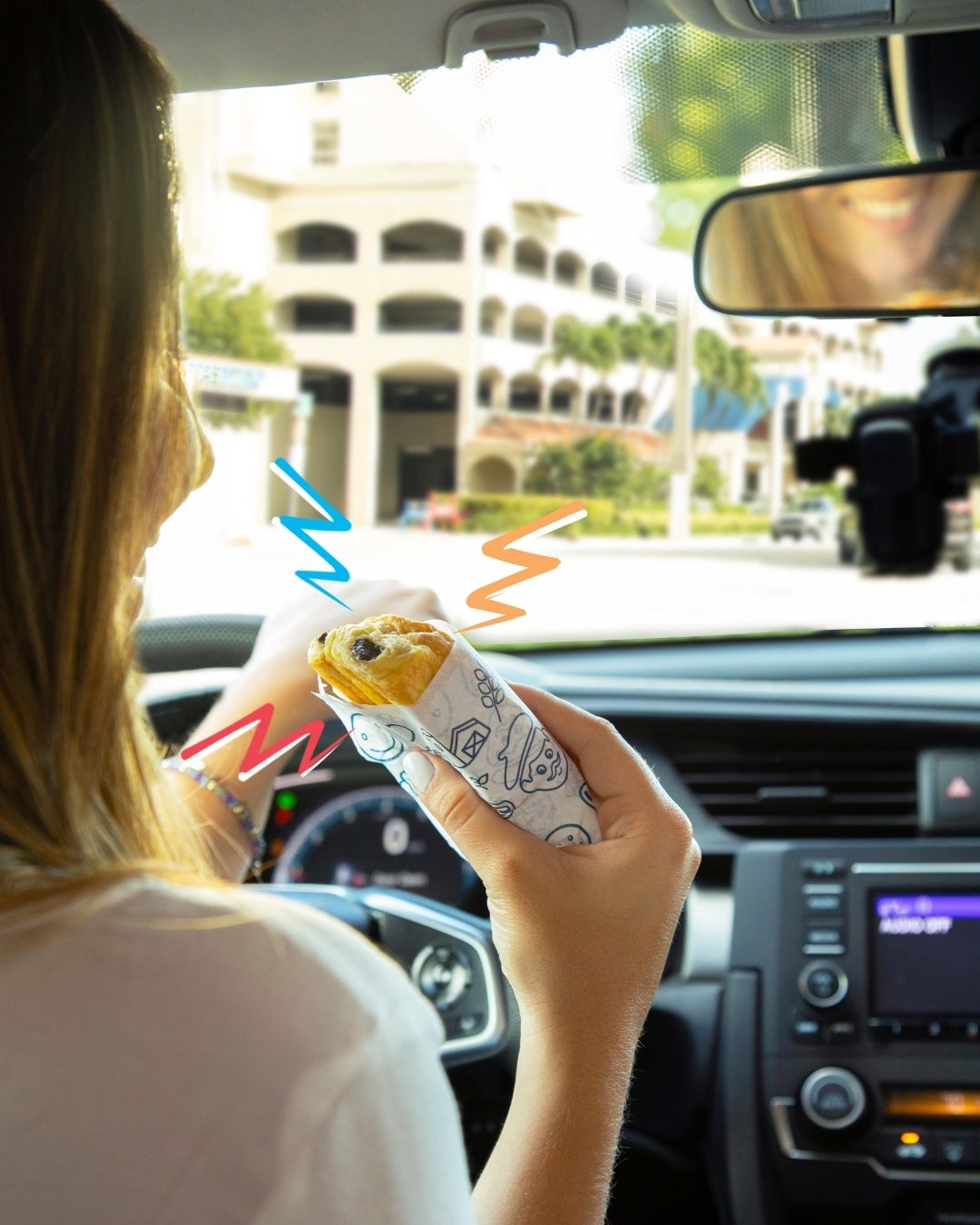 A woman eating a chocolate croissant from bakerly in the car (Snack Time: Unwrap et Voilà With These Snacks From Bakerly Lynda Lantz Contributor Miami Mom Collective)
