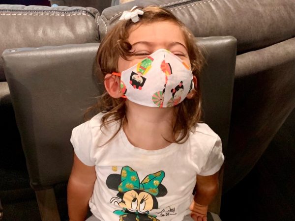A little girl smiling behind her mask (Wear a Mask: How To Get Your Toddler to Wear One (and Keep It On!) Alexa Gonzalez Contributor Miami Mom Collective)