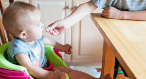 An older sibling feeds a toddler a cracker