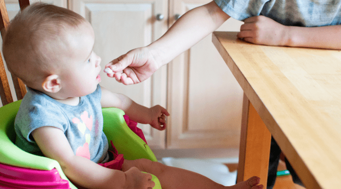 An older sibling feeds a toddler a cracker
