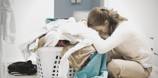 An overwhelmed mom leaning over a basket of laundry (A Letter to Moms as We Stumble Into 2021: There is Hope by Lindsay K. Madsen, Miami Mom Collective)