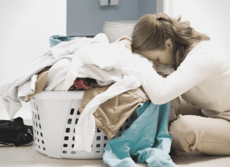 An overwhelmed mom leaning over a basket of laundry (A Letter to Moms as We Stumble Into 2021: There is Hope by Lindsay K. Madsen, Miami Mom Collective)