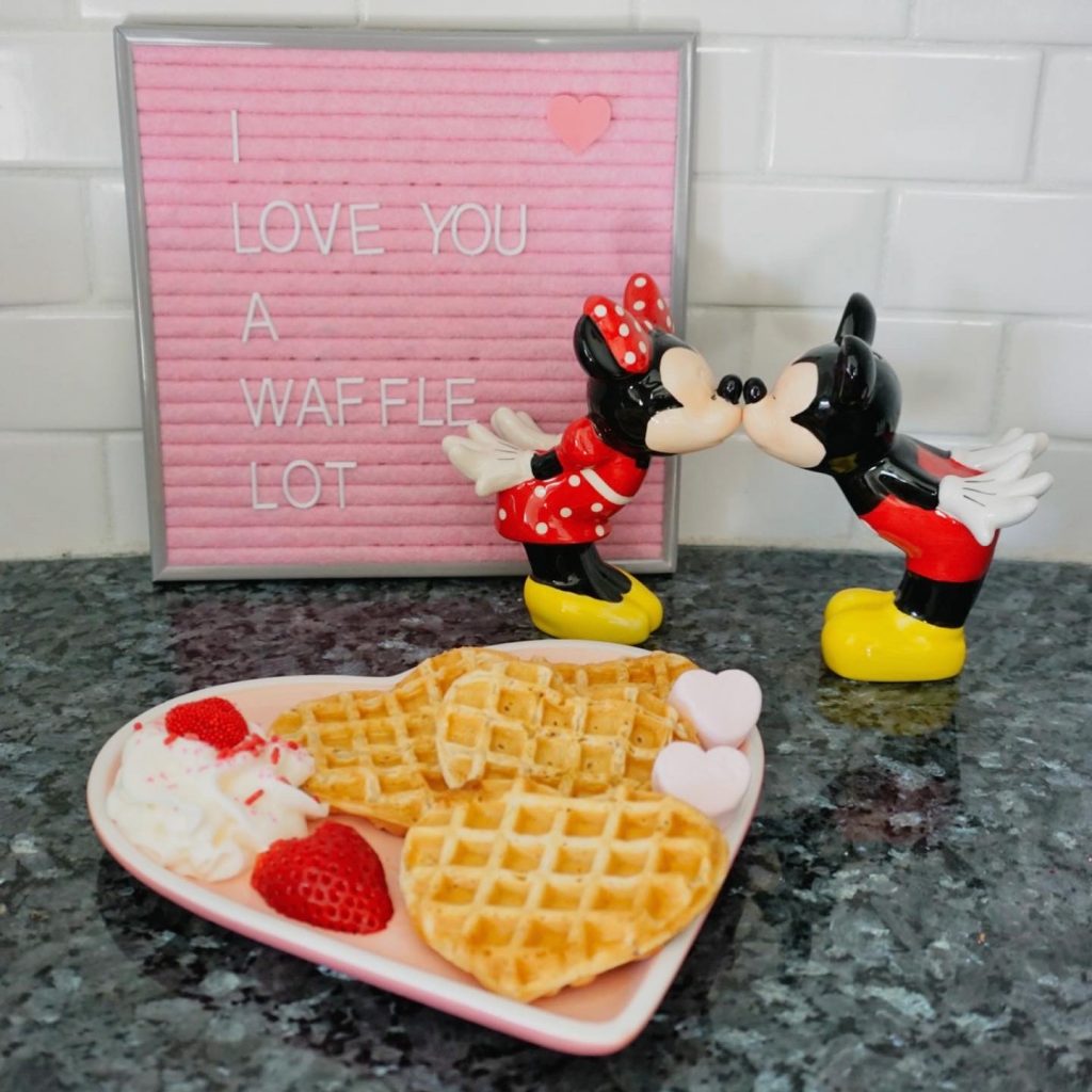 "I love you a waffle lot" sign with Mickey Mouse & Minnie Mouse, and a plate of heart-shaped waffles