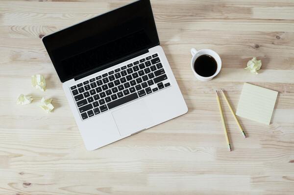 Image: A laptop, cup of coffee, pencils, and Post-It notes on a table