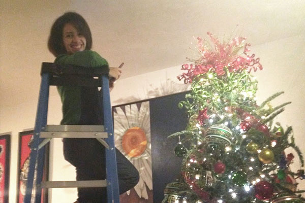 women in ladder next to top of christmas tree