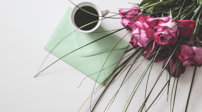 Image: A sealed envelope on a table with a cup of coffee and bouquet of roses