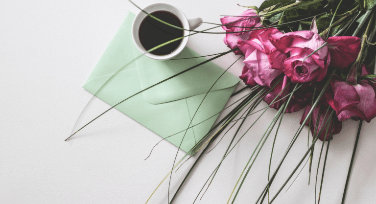 Image: A sealed envelope on a table with a cup of coffee and bouquet of roses