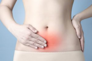 Image: A woman's torso with one hand on her hip and one hand placed over her lower abdomen