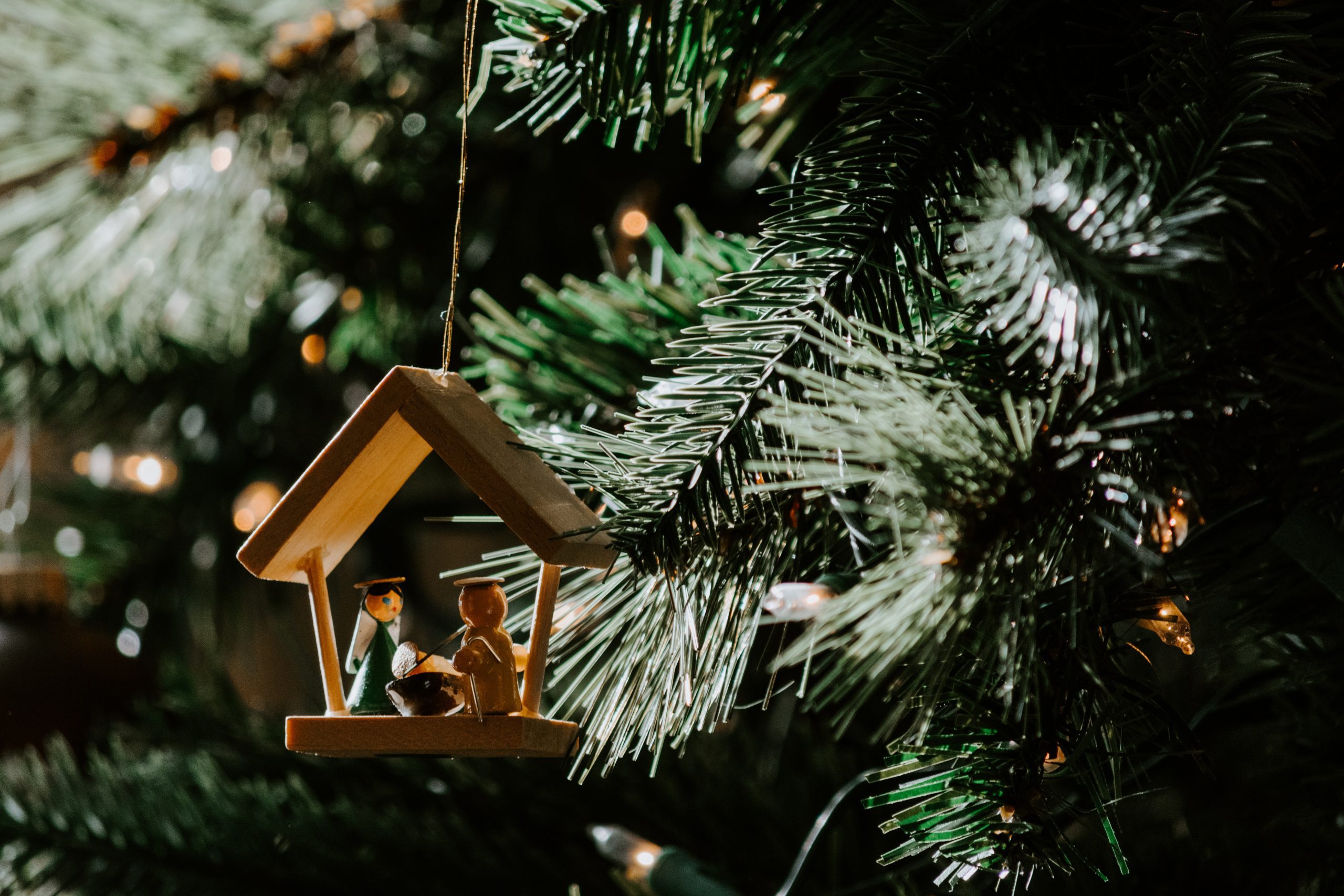 A nativity ornament hanging on a Christmas tree