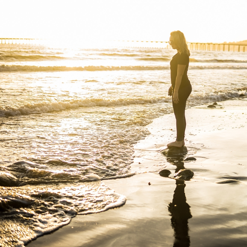 Image: A woman standing on the shoreline, watching the waves