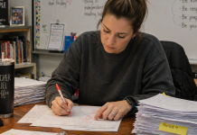 A tired teacher is grading a large stack of papers on her desk.