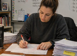 A tired teacher is grading a large stack of papers on her desk.
