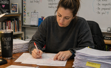 A tired teacher is grading a large stack of papers on her desk.