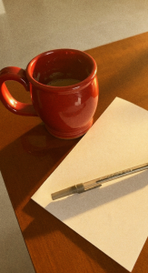 Image: A coffee mug on a table next to a blank sheet of paper and a pen