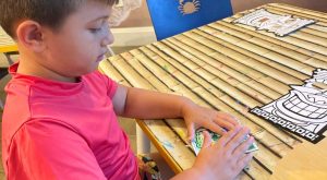 Image: A child sits at a table and works on a craft activity
