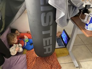 Image: Two children watch a movie on a device in a play fort on the floor