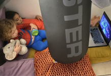 Image: Two children watch a movie on a device in a play fort on the floor