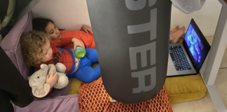 Image: Two children watch a movie on a device in a play fort on the floor