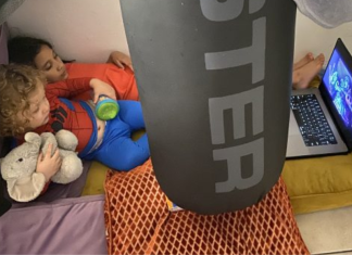 Image: Two children watch a movie on a device in a play fort on the floor