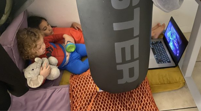 Free Indoor Activities for Kids: A Real Take on At-Home Adventure Image: Two children watch a movie on a device in a play fort on the floor