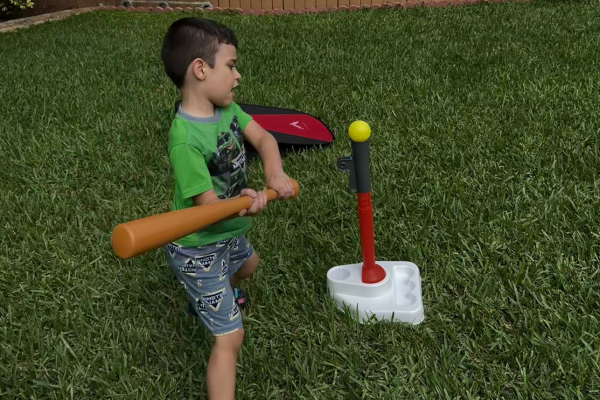 A young boy is swinging a plastic bat at a t-ball stand.