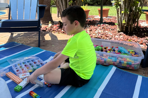 A young boy is playing with numberblocks snap cubes outside on a picnic mat.