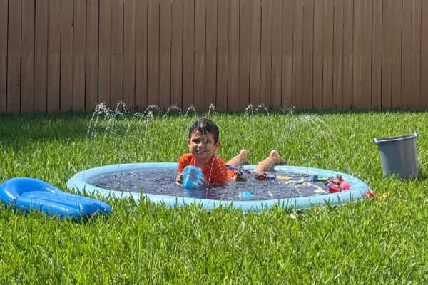 A young boy is laying on his stomach in a splash pad in the backyard.