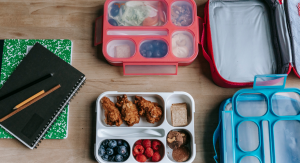 Image: Two open lunchboxes containing school lunch options on a table next to a stack of notebooks