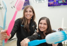 All Smiles Pediatric Dentistry: Comfort, Care & Community Image: Dr. Smith and Dr. Lenard of All Smiles Pediatric Dentistry smile for the camera, each holding a large colorful toothbrush
