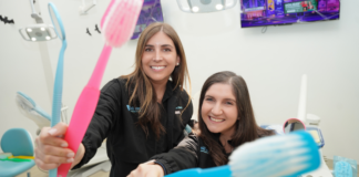 All Smiles Pediatric Dentistry: Comfort, Care & Community Image: Dr. Smith and Dr. Lenard of All Smiles Pediatric Dentistry smile for the camera, each holding a large colorful toothbrush